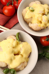 Bowls of delicious cauliflower with cheese sauce and vegetables, closeup