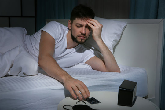 Handsome Young Man Going To Take Pills Against Headache While Lying In Bed At Night