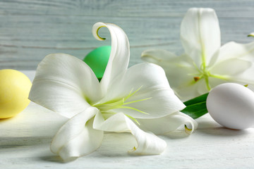 Fototapeta na wymiar Beautiful composition with white lilies and Easter eggs on wooden background