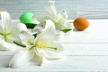 Fototapeta na wymiar Beautiful composition with white lilies and Easter eggs on wooden background