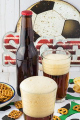 Bottle of beer and glasses full of bear on the table decorated for soccer party.