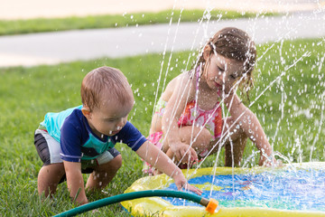 Kids or children playing with water on a warm summer day in the garden