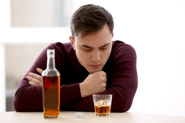 Handsome depressed man drinking whisky at home