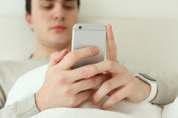 Young man with sleep tracker and mobile phone lying in bed at home, closeup