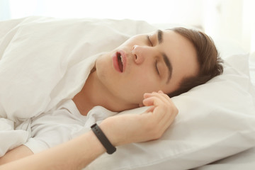 Young man with sleep tracker resting in bed at home