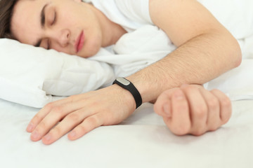 Young man with sleep tracker resting in bed at home