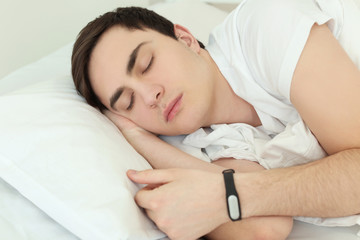 Young man with sleep tracker resting in bed at home
