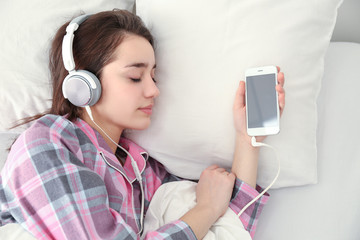 Young woman listening to music in headphones on bed