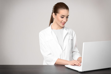 Young woman pharmacist standing at table on grey background