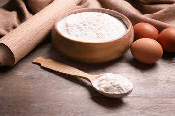 Bowl with flour, roller pin, eggs and spoon on wooden table