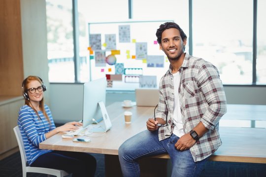 Male sitting on desk with coworker in conference