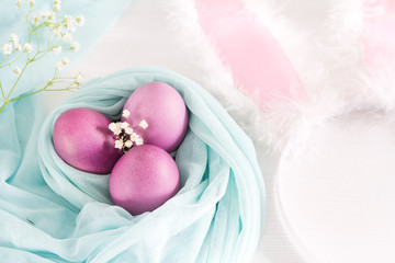 Colorful easter eggs and rim hare ears on a white wooden background. Selective focus and space for text.