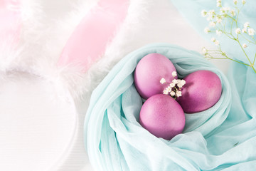 Colorful easter eggs and rim hare ears on a white wooden background. Selective focus and space for text.