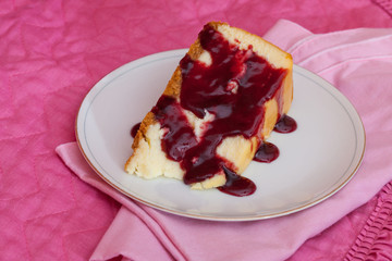 A slice of cheesecake with raspberry sauce on a white plate with a pink napkin and place mat.