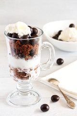 Layered dessert with with a filbert in chocolate, a biscuit, a chocolate crumb and creamy ice cream in glass jar, selective focus