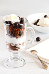 Layered dessert with with a filbert in chocolate, a biscuit, a chocolate crumb and creamy ice cream in glass jar, selective focus