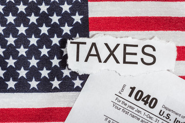 1040 tax form with word taxes in torn paper on American Flag