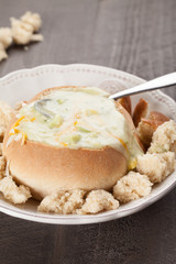 Creamy Broccoli Cheddar Soup in Large Baked Homemade Roll on white plate on dark wooden background with torn bread pieces