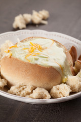 Creamy Broccoli Cheddar Soup in Large Baked Homemade Roll on white plate on dark wooden background vertical shot