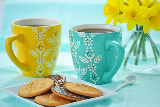 Mugs of coffee with biscuits and daffodils