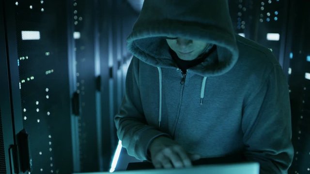  High Angle Shot of Computer Hacker in Hoodie, Holding Laptop. He Breaked in a Corporate Data Center. Shot on RED EPIC-W 8K Helium Cinema Camera.