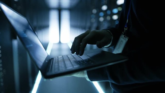 IT Specialist Working Working on a Laptop, He's Employee of  Big Ultramodern Data Center. Shot on RED EPIC-W 8K Helium Cinema Camera.