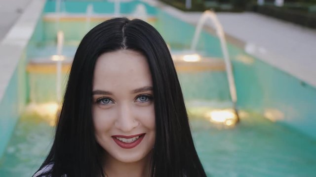 Portrait of flirting young woman. Cheerful happy girl looking at camera, talking, laughing on illuminated fountain background.