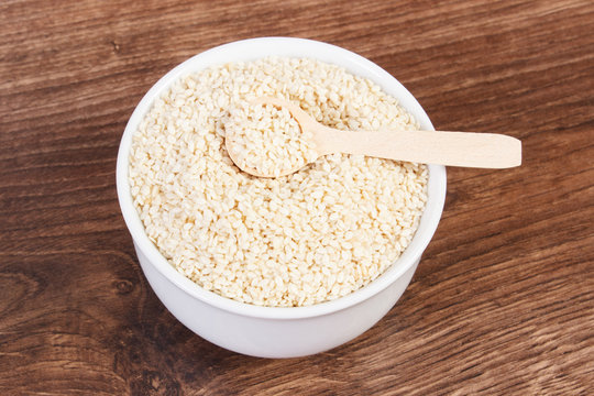 Heap of sesame seeds in white bowl on wooden board