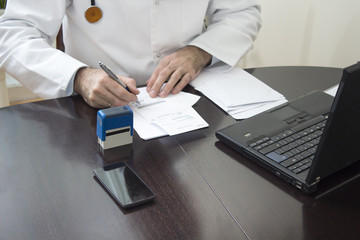 Lekarz w białym kitlu siedzi przy stole i przystawia pieczątkę do dokumentu. Ręce lekarza przystawiającego pieczątkę na recepcie. Lekarz wypisuje receptę przy biurku. - obrazy, fototapety, plakaty