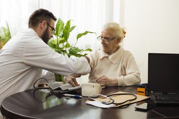Dłoń starej kobiety na ciemnym tle. Badanie lekarskie. Lekarz trzyma dłoń starej kobiety Bardzo stara kobieta siedzi przy stole. Lekarz podwija rękaw i przygotowuje do badania.