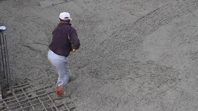 Worker smoothing the concrete surface of basement floor slabs. Concrete rake does a better job smoothing out chunky concrete mix