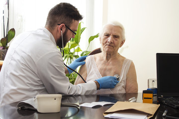 Fototapeta Lekarz bada stetoskopem starą kobietę w gabinecie lekarskim. Badanie lekarskie stetoskopem. Lekarz geriatra bada płuca. obraz