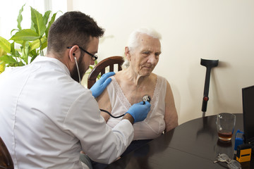 Lekarz bada stetoskopem starą kobietę w gabinecie lekarskim. Badanie lekarskie stetoskopem. Lekarz geriatra bada płuca. - obrazy, fototapety, plakaty