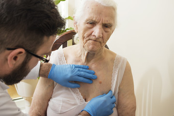 Lekarz geriatra podczas badania. Lekarz bada zmiany na skórze u starej kobiety. - obrazy, fototapety, plakaty
