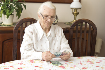 Staruszka liczy pieniądze siedząc przy stole. Emerytura. Stara kobieta liczy pieniądze. - obrazy, fototapety, plakaty
