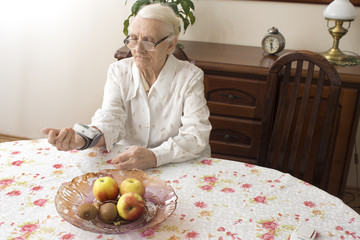 Staruszka mierzy ciśnienie tętnicze siedząc w salonie przy stole. Stara kobieta mierzy...