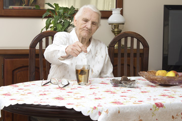 Stara kobieta siedzi przy stole w salonie i parzy herbatę w szklance.