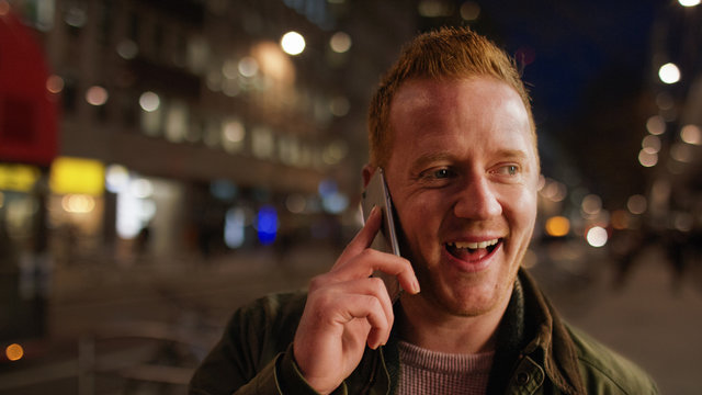 Young Man Walking Through The City At Night And Talking On His Phone