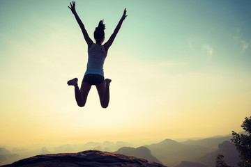 young woman jumping on sunrise rocky mountain peak, freedom, risk, challenge, success concept