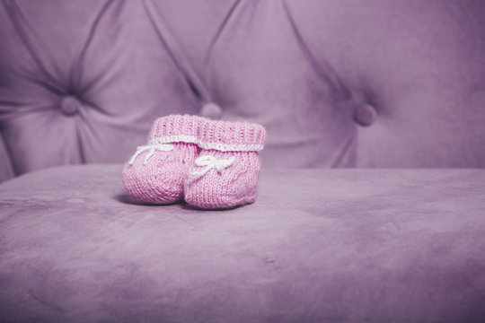 Pink knitted baby booties closeup standing on the couch