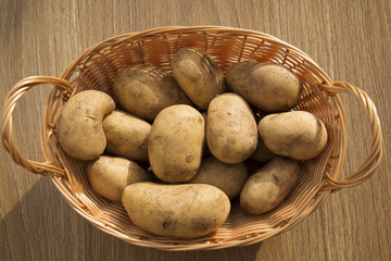Obraz na płótnie Canvas Raw potatoes in a basket on a wooden table