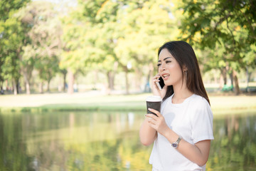 Young beautiful woman holding disposable coffee cup while talking on phone at nature outdoors Women lifestyle concept.