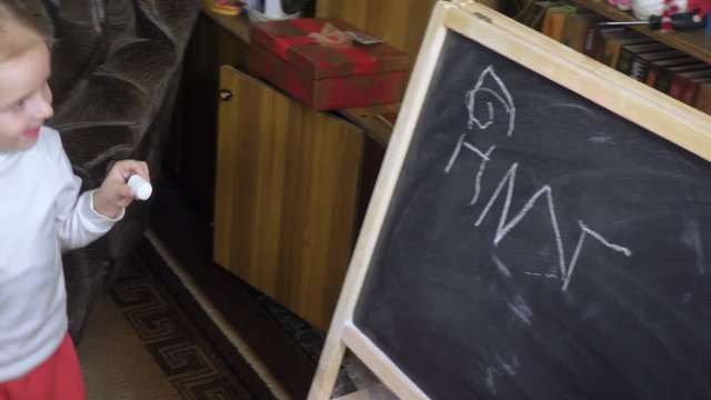 Little girl draws chalk on blackboard