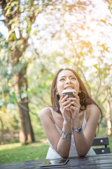 Young woman holding disposable coffee cup while sitting enjoying at nature outdoors.