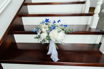 Lush wedding bouquet of white peonies, blue flowers and eucalyptus is on the wooden stairs