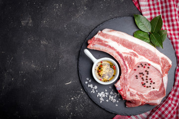 Raw meat with herbs, oil and spices on dark background with copy space. Raw pork steak. Ingredients for cooking meat. Top view