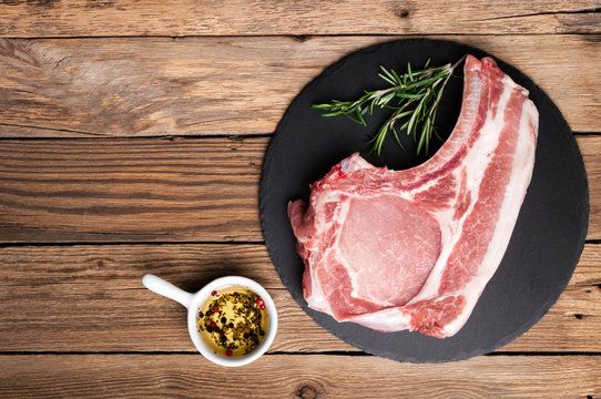 Raw meat on rustic wooden background. Raw pork steak with herbs, oil and spices. Cooking meat. Copy space. Top view