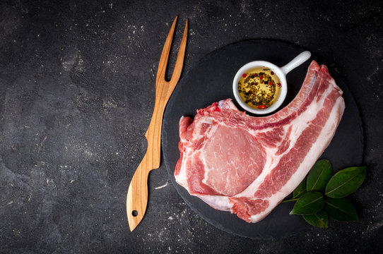 Raw meat with herbs, olive oil and spices on dark background with copy space. Raw pork steak. Ingredients for cooking meat. Top view
