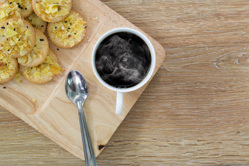 Black coffee in white cup and cookies is all in the wooden tray on brown wooden table