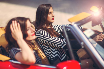 Portrait of two beautiful sexy fashion woman model sitting in luxury retro cabriolet car
